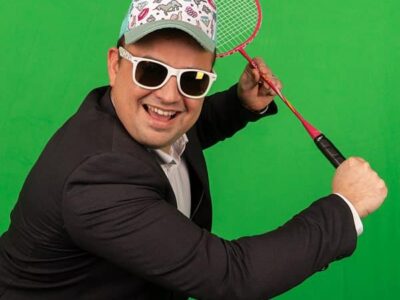 Homme en costume, jouant badminton, fond vert.