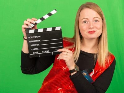 Femme tenant un clap de cinéma, fond vert.