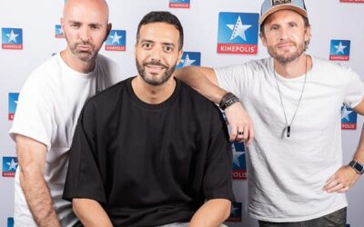 Trois hommes posent devant panneau Kinepolis.