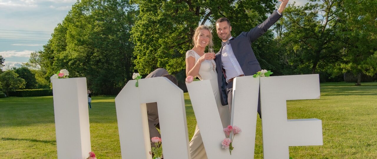 Couple joyeux devant lettres LOVE décorées de fleurs.