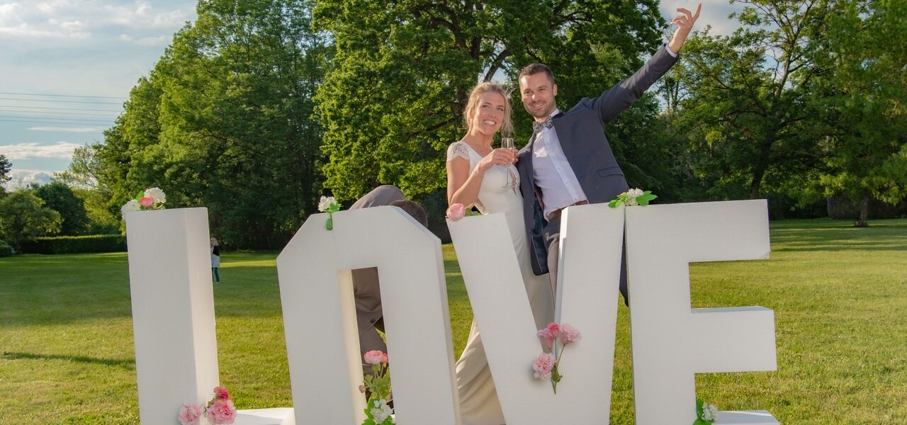 Couple joyeux devant lettres LOVE décorées de fleurs.