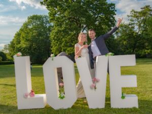 Couple joyeux devant lettres LOVE décorées de fleurs.