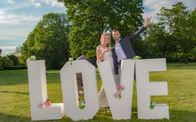 Couple joyeux devant lettres LOVE décorées de fleurs.