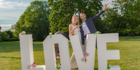 Couple joyeux devant lettres LOVE décorées de fleurs.