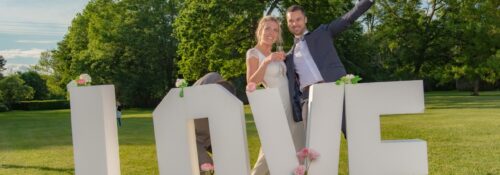 Couple joyeux devant lettres LOVE décorées de fleurs.