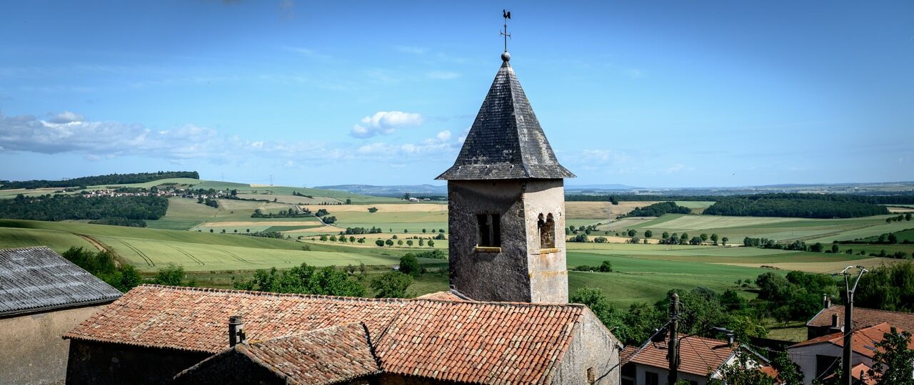 Église et campagne vallonnée sous ciel bleu.