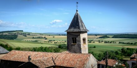 Église et campagne vallonnée sous ciel bleu.