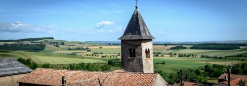 Église et campagne vallonnée sous ciel bleu.
