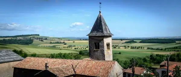 Église et campagne vallonnée sous ciel bleu.