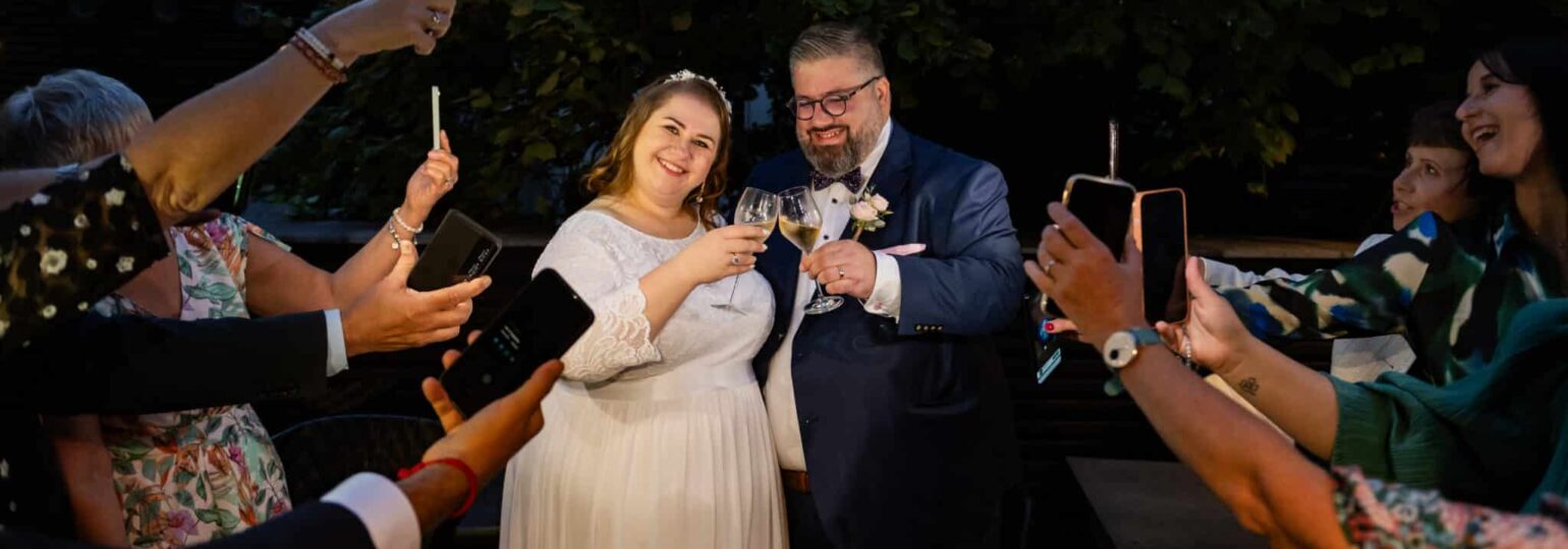 Mariage, couple trinque, invités prennent photos.