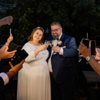 Mariage, couple trinque, invités prennent photos.