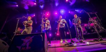 Groupe de musiciens en concert avec éclairage violet.