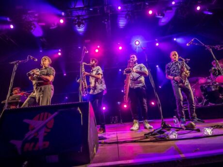 Groupe de musiciens en concert avec éclairage violet.