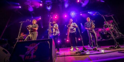 Groupe de musiciens en concert avec éclairage violet.