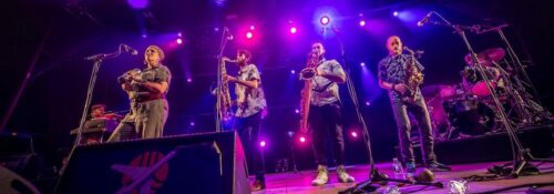 Groupe de musiciens en concert avec éclairage violet.