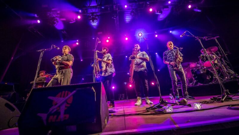 Groupe de musiciens en concert avec éclairage violet.