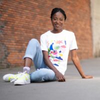 Personne souriante en t-shirt graphique assise contre un mur.