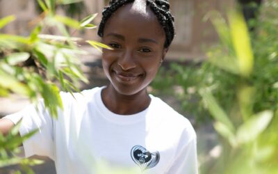 Femme souriante en t-shirt blanc parmi les plantes.