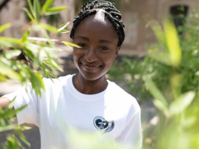 Femme souriante en t-shirt blanc parmi les plantes.