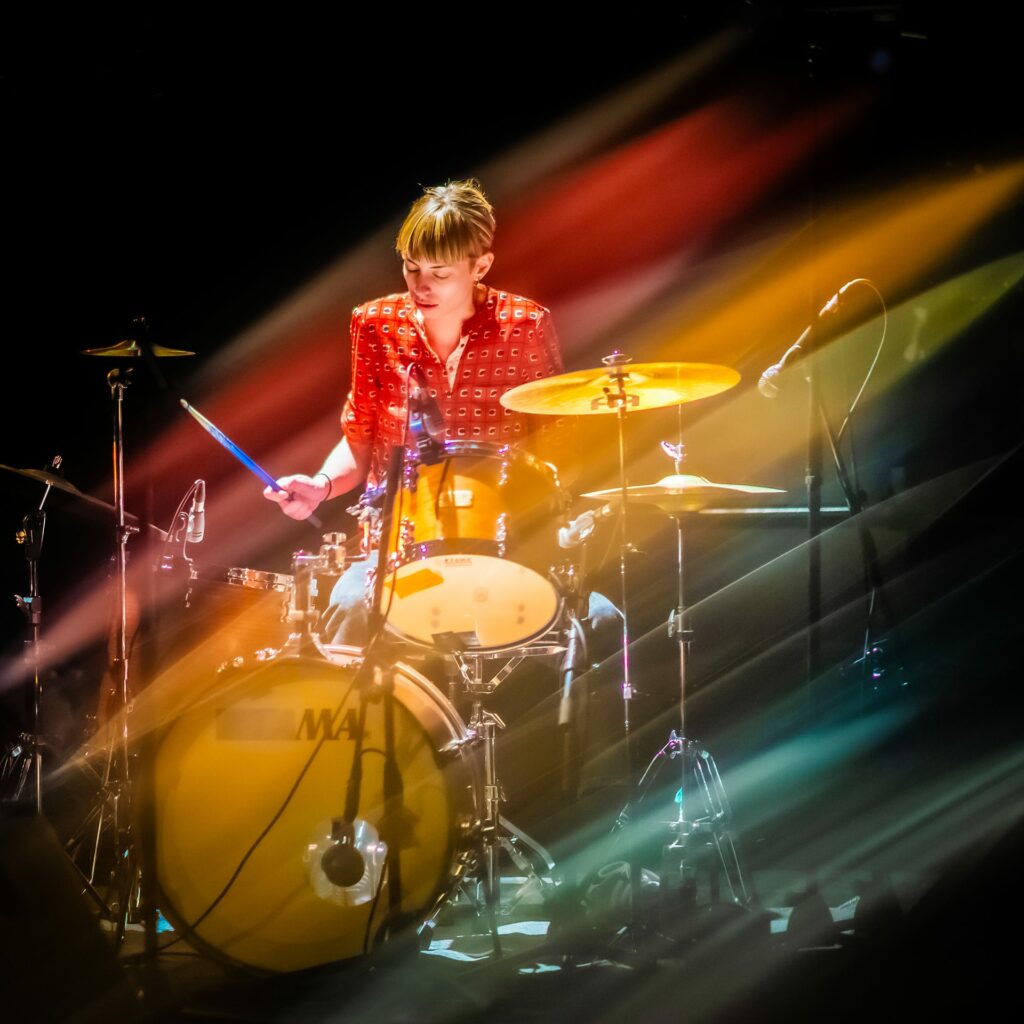 Musicienne jouant de la batterie sur scène colorée.