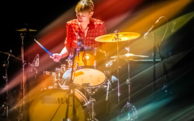 Musicienne jouant de la batterie sur scène colorée.