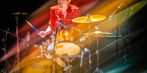 Musicienne jouant de la batterie sur scène colorée.