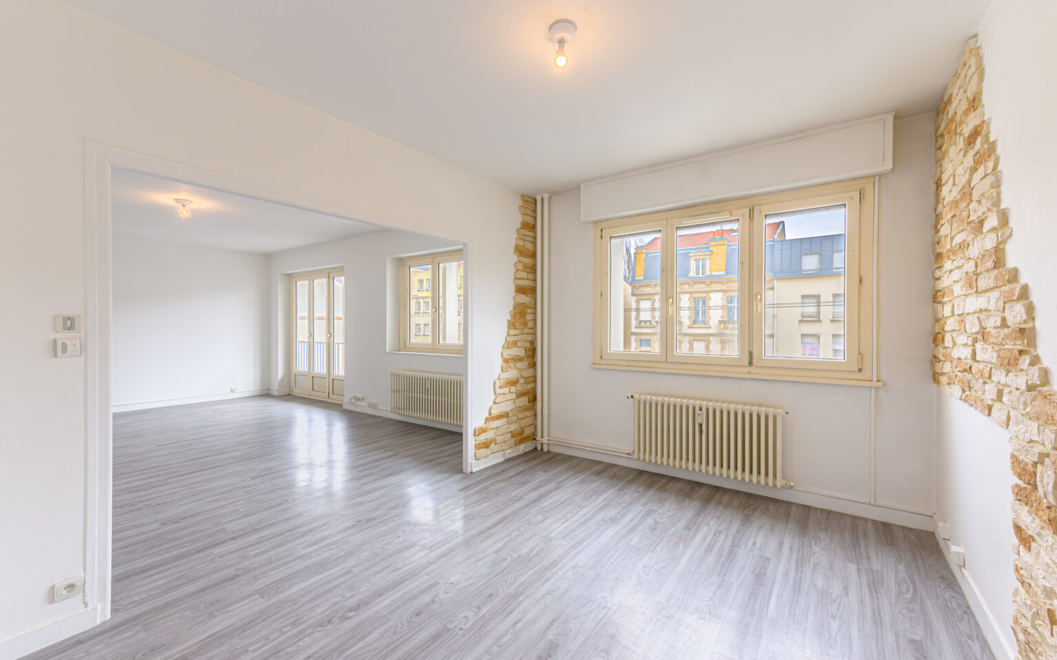 Salon lumineux avec parquet et murs partiellement en pierre.