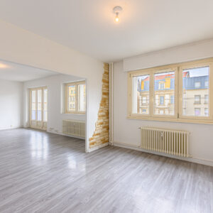 Salon lumineux avec parquet et murs partiellement en pierre.