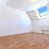 Chambre mansardée avec parquet et fenêtre de toit.