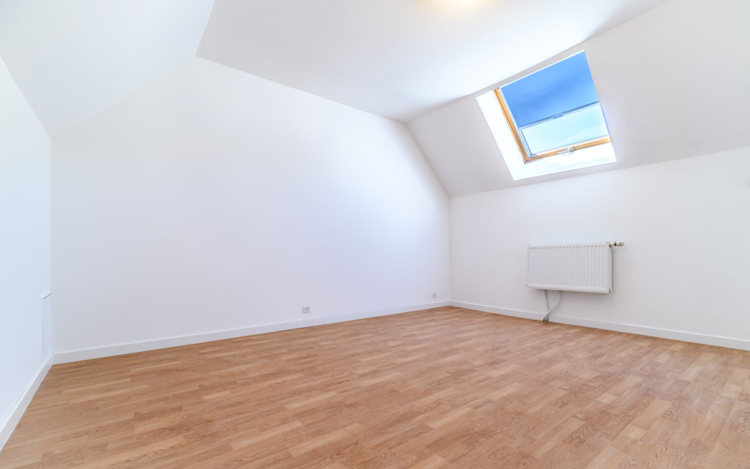 Chambre mansardée avec parquet et fenêtre de toit.