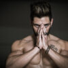 Homme musclé concentré mains jointes devant visage.