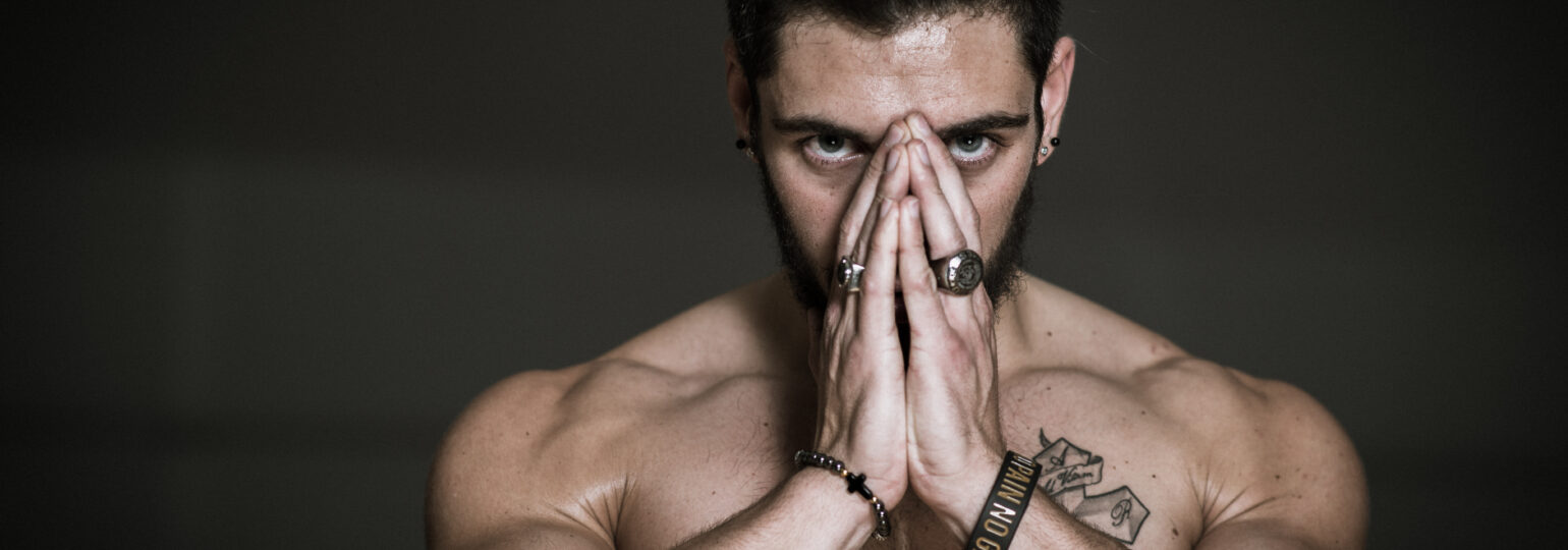 Homme musclé concentré mains jointes devant visage.