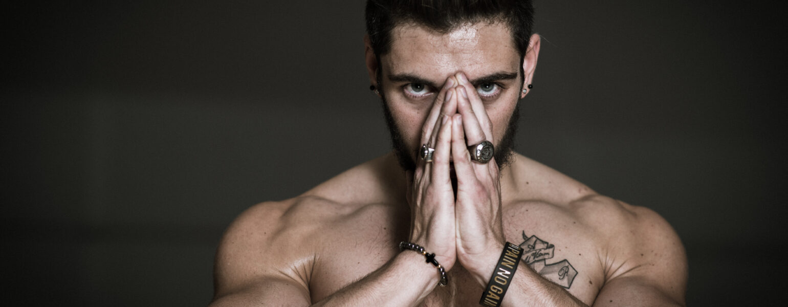 Homme musclé concentré mains jointes devant visage.
