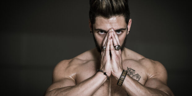 Homme musclé concentré mains jointes devant visage.