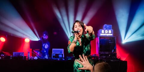 Chanteuse sur scène avec éclairage vibrant et DJ.