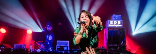 Chanteuse sur scène avec éclairage vibrant et DJ.