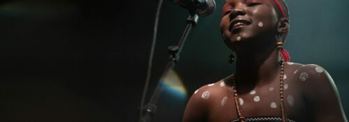 Chanteuse sur scène, micro et décorations corporelles.