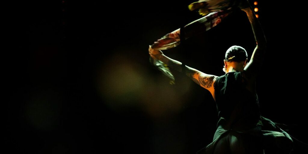 Danseuse avec foulard coloré sur scène sombre.