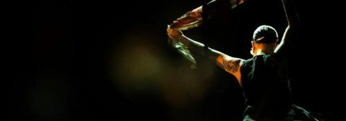 Danseuse avec foulard coloré sur scène sombre.