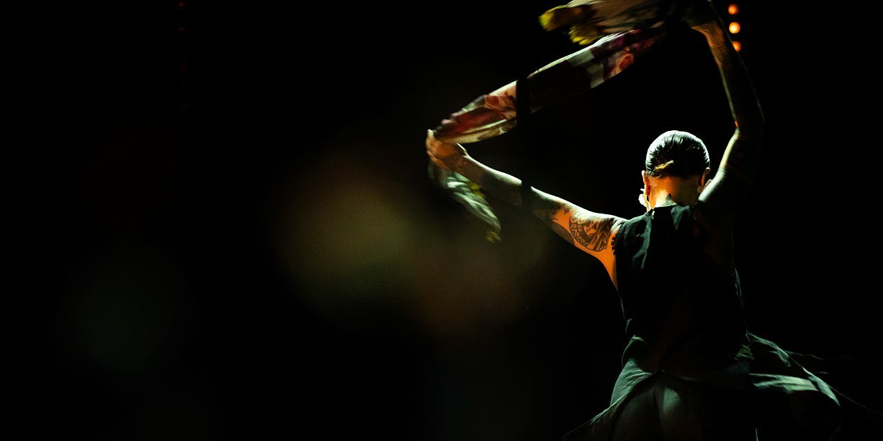 Danseuse avec foulard coloré sur scène sombre.