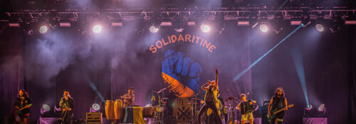 Concert avec éclairage coloré et décor 'Solidaritine'.