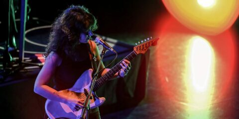 Musicienne chante sur scène avec guitare électrique.