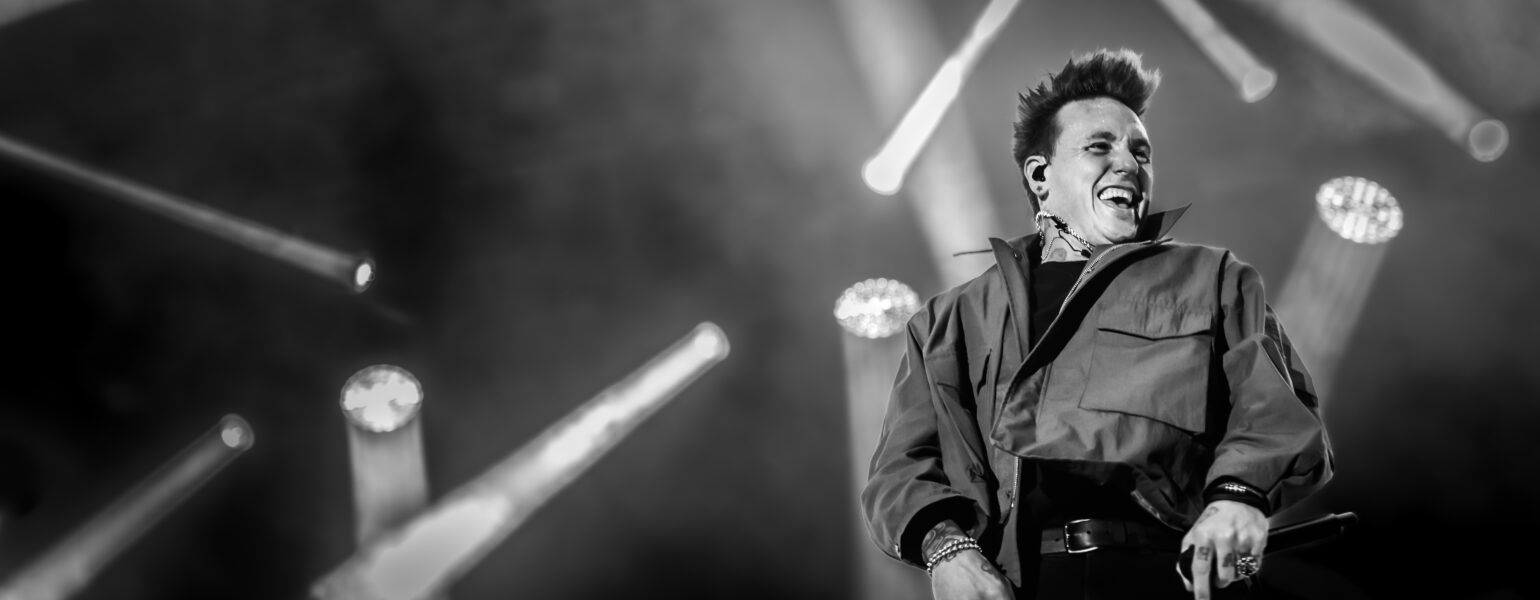 Chanteur souriant sur scène en concert noir et blanc.