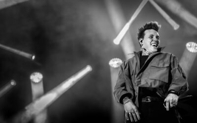Chanteur souriant sur scène en concert noir et blanc.