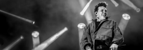 Chanteur souriant sur scène en concert noir et blanc.