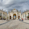 Arc monumental sur une place pavée, ciel nuageux.
