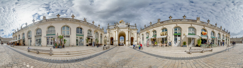 Arc monumental sur une place pavée, ciel nuageux.