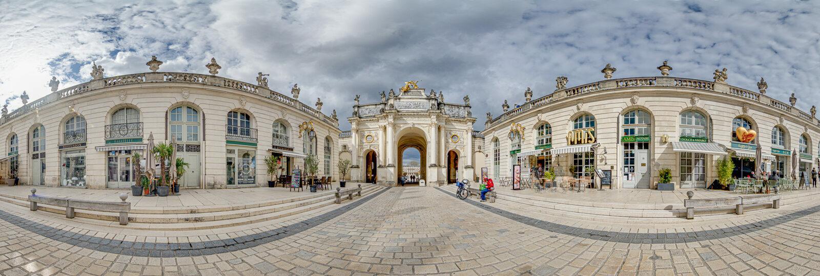 Arc monumental sur une place pavée, ciel nuageux.