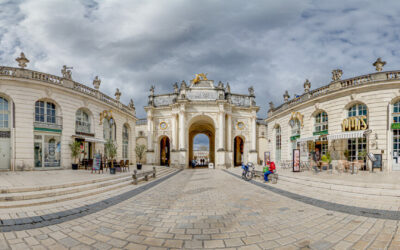 Arc monumental sur une place pavée, ciel nuageux.