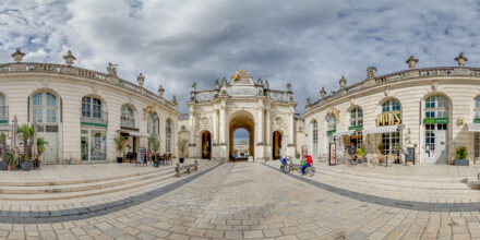 Arc monumental sur une place pavée, ciel nuageux.